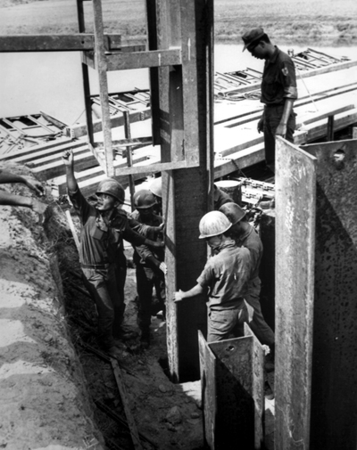 PICTURE - CORPORAL MUNG, 103d Engr. Bn., ARM, directs his construction crew in pile driving for a new bridge.