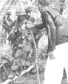 Photograph: Combat Photographer Of 221st Signal Company Gets A Helping From Vietnamese Civilian