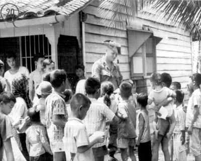 Photo:  U.S. CIVIC ACTION OFFICER FROM THE 199TH LIGHT INFANTRY BRIGADE GIVING TREATS TO THE CHILDREN. In the same house, medical facilities have been set up to treat the sick.