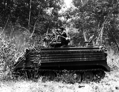 PICTURE - M113 IN ACTION AT BEN CUI RUBBER PLANTATION, AUGUST 1968. Hollow steel planking on sides of vehicle offer protection against shaped charges.